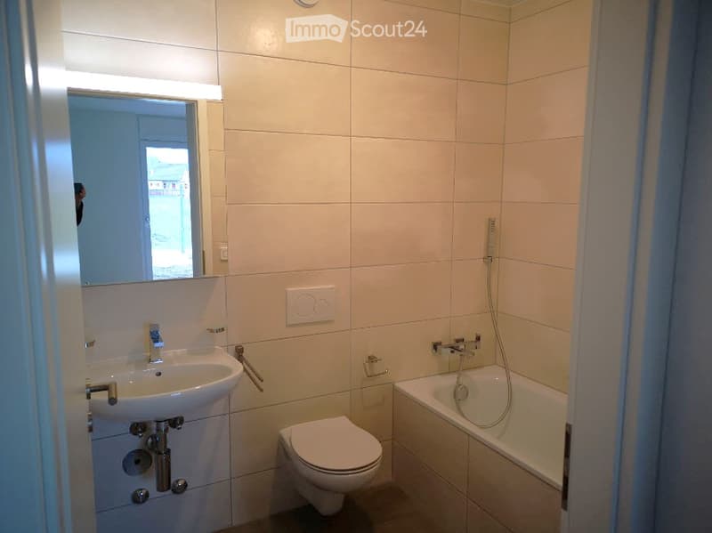 Modern bathroom with white tiles, a sink, toilet, bathtub, and a large mirror above the sink.