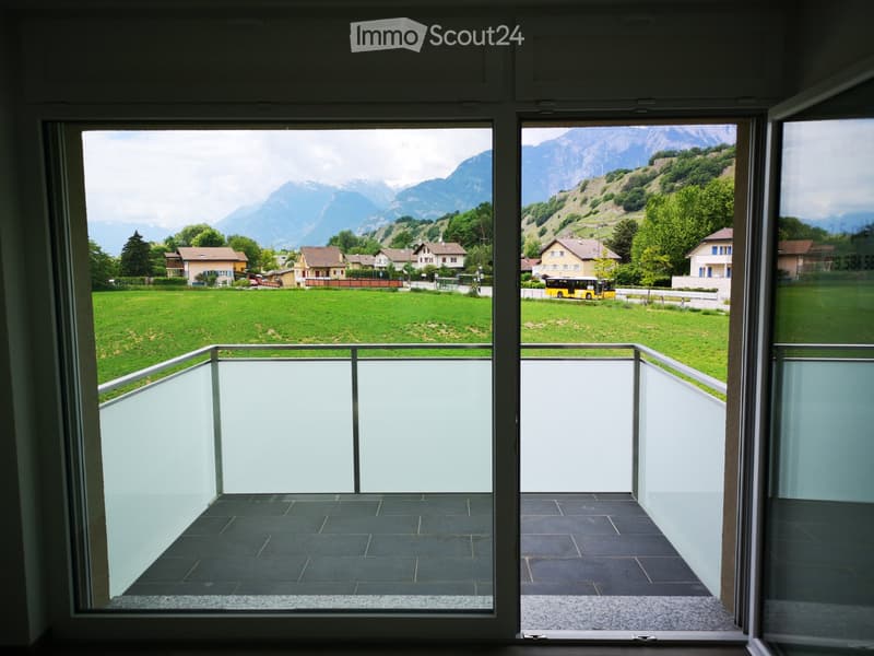 Balcony with modern glass railing, dark tiled floor, and expansive view of green fields, houses, and mountains.