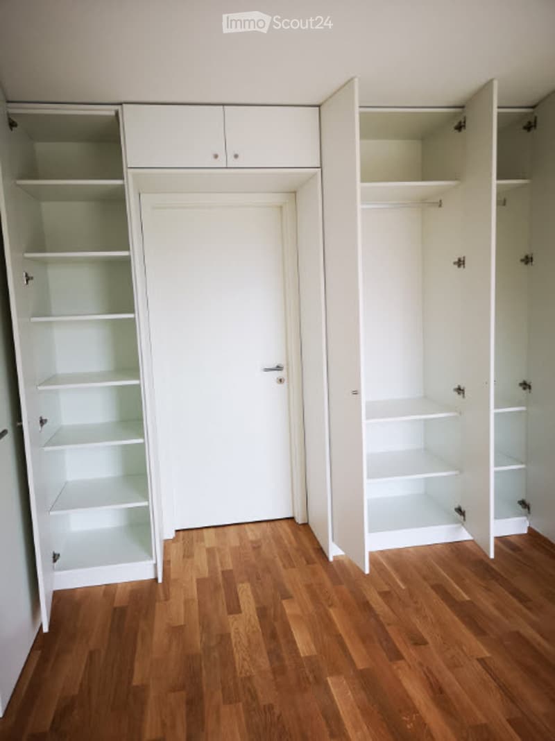Empty room with wooden flooring, white walls, and built-in white closet units with open shelves.