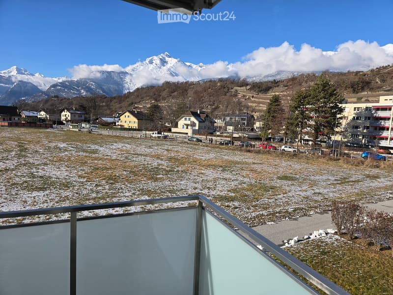Balcony overlooking a snow-covered field with a town and snow-capped mountains in the background.