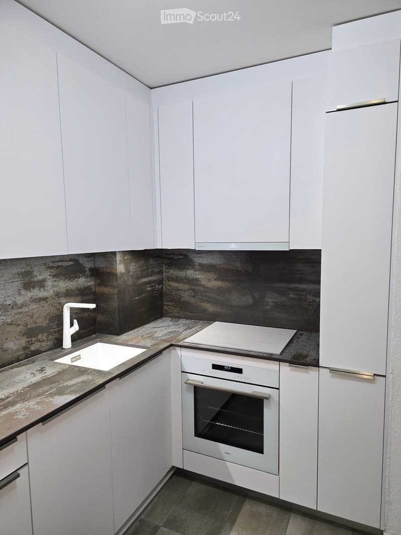 Modern kitchen with white cabinets, stainless steel appliances, and a dark, textured backsplash.