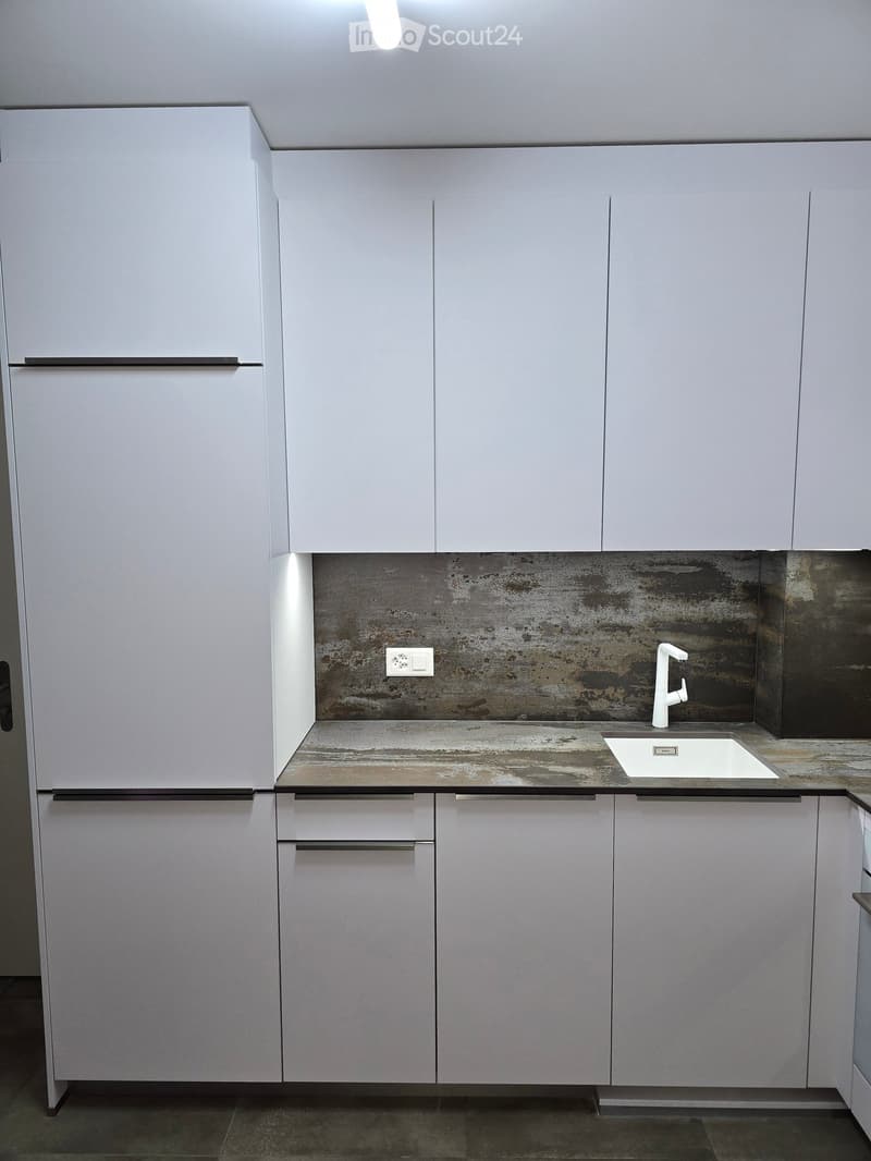 Modern kitchen with white cabinets, a concrete-style backsplash, and a white sink with a modern faucet.