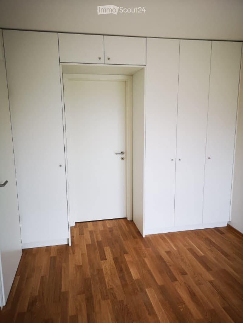 Completely empty room with white walls, wooden floor, and built-in white wardrobes.