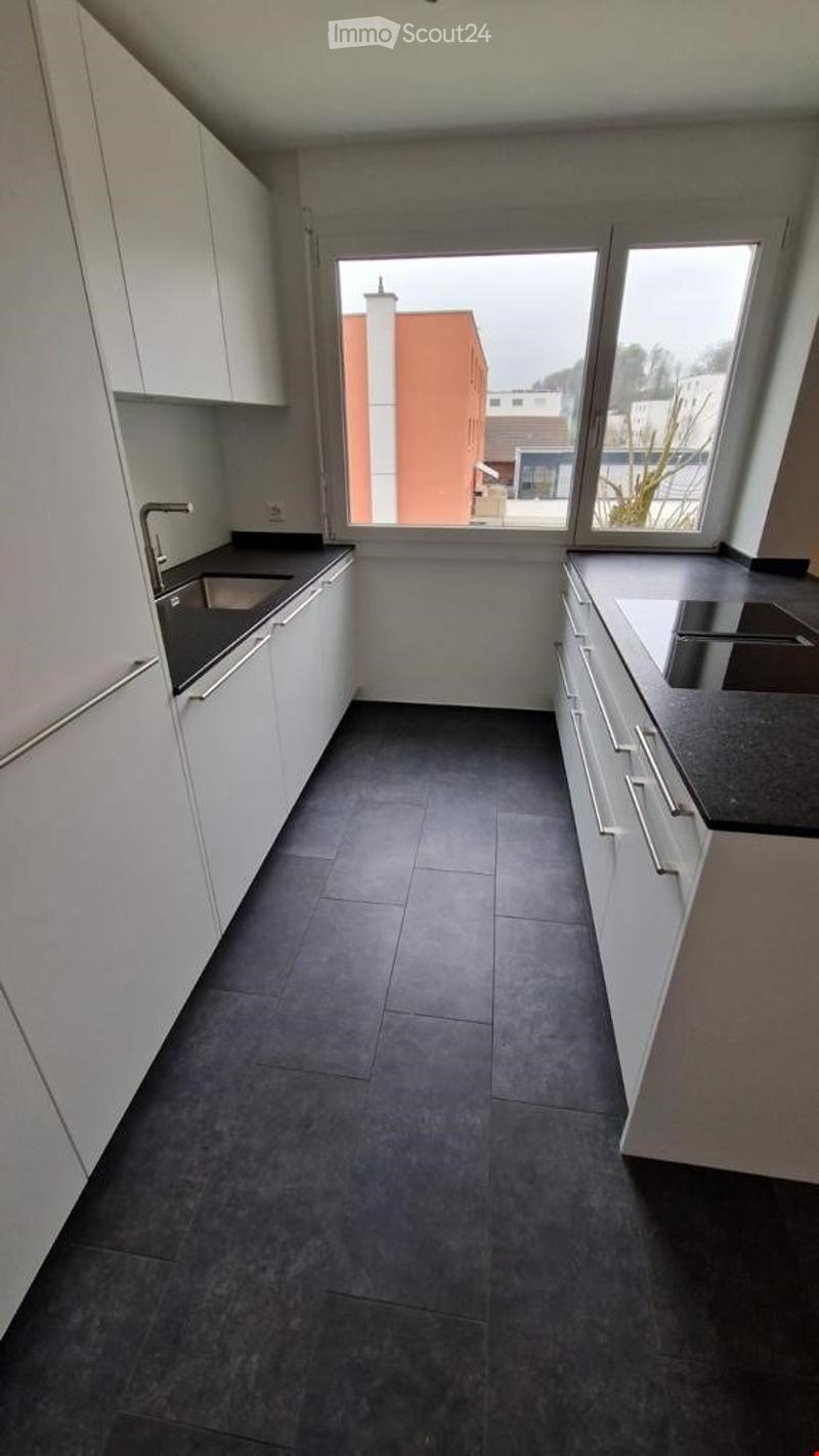 Modern kitchen with white cabinets, dark countertops, and a large window overlooking a building exterior.