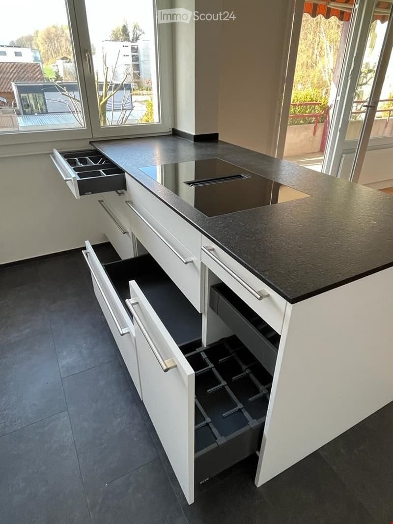 Modern kitchen island with white cabinets, black countertop, and multiple open drawers.