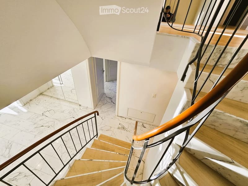 Spiral staircase with wooden steps and marble landing, featuring black metal railings and warm lighting.