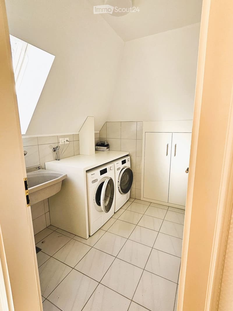 Clean, modern bathroom with a washing machine, sink, and white cabinets.