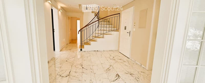 Spacious hallway with marble flooring, white walls, recessed lighting, and a curved staircase with a metal railing leading to an upper level.