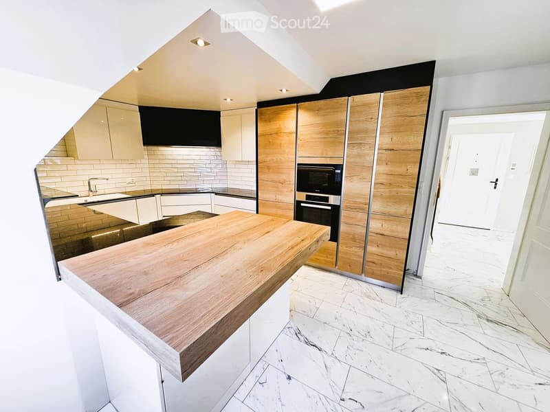 Modern kitchen with a wooden countertop, built-in oven, sink, and light-colored cabinets. The floor is marble, and the walls feature a combination of white tiles and dark panels.