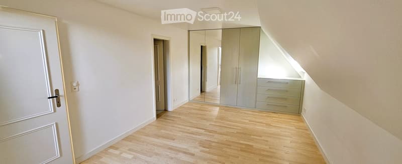 Empty room with light wooden flooring, white walls, and a large mirrored wardrobe with drawers. No furniture or personal items are present.