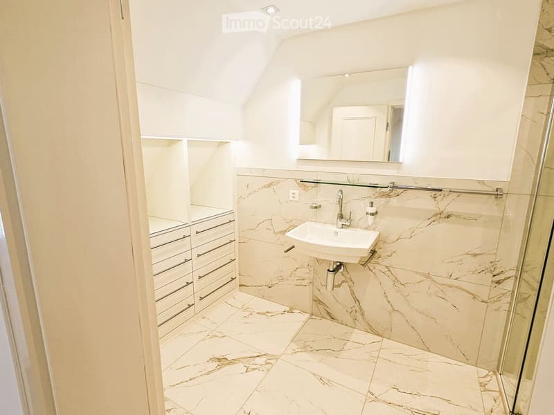 Modern bathroom with marble tiles, white sink, mirrored cabinet, and built-in storage drawers.