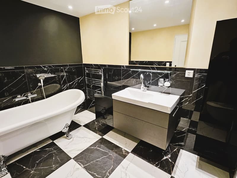 Modern bathroom with black marble tiles, a freestanding bathtub, a sink with a modern faucet, a large mirror, and a radiator.
