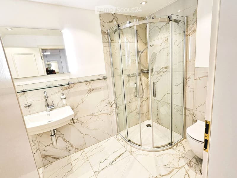 Modern bathroom with marble tiles, a walk-in shower with glass enclosure, a white sink, and a toilet.