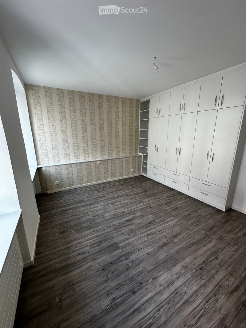 Empty room with wooden flooring, white built-in wardrobes, and a textured wall design. No furniture or personal items are present.