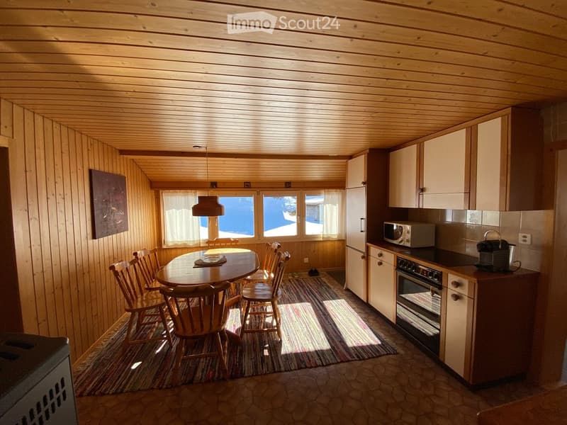 Cozy kitchen and dining area with wooden walls and ceiling, a round dining table with chairs, and modern appliances including a refrigerator, microwave, and oven.