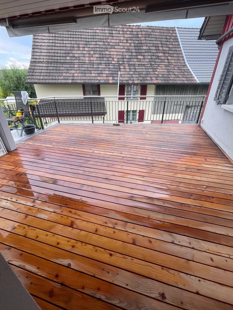 Wooden deck with metal railing, overlooking a neighboring house with red shutters and a tiled roof.