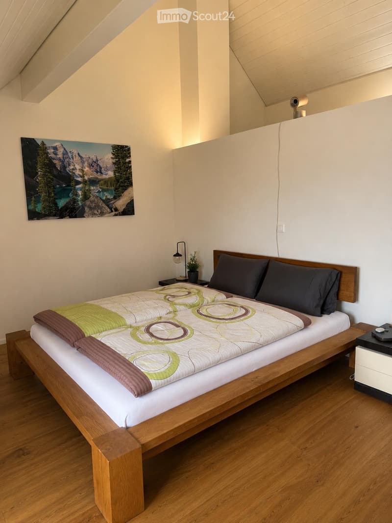 Cozy bedroom with a wooden bed, green and brown bedding, nightstands, a lamp, and a scenic picture on the wall.