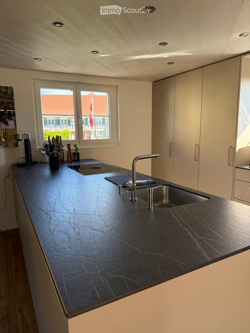 Modern kitchen with a dark marble countertop, stainless steel sink, and sleek white cabinets. A knife block and various kitchen items are placed on the counter.