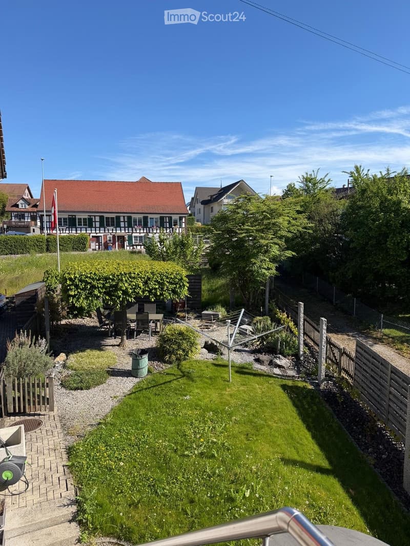 Well-maintained garden with a lawn, patio furniture, a clothesline, and surrounding fences. The area is bordered by gravel paths and includes a small shed and a trash can.