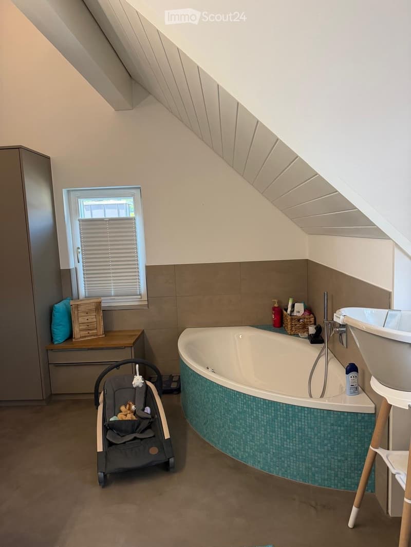 Bathroom with a bathtub, sink, small wooden stool, baby chair, and various toiletries on the edge of the tub.