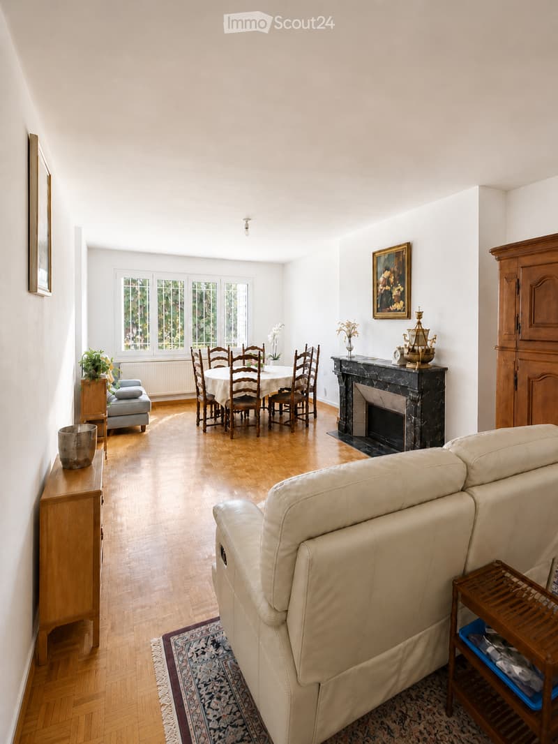 Bright living and dining area with hardwood floors, a cream-colored sofa, a fireplace, a dining table with chairs, and decorative items.