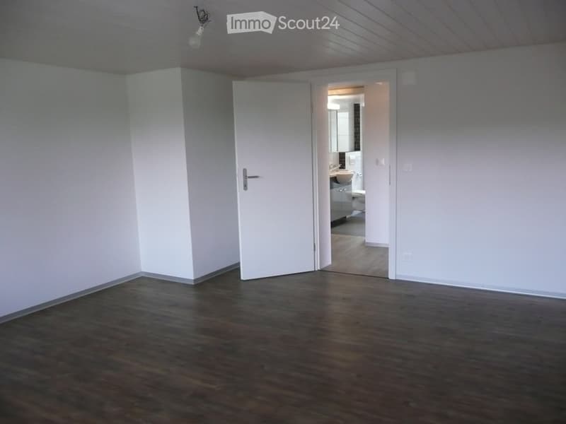 empty room, white walls, wooden floor, an open door leading to bathroom