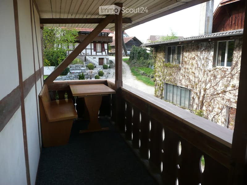 Wooden table and chair on balcony, wooden railing, view of path and neighboring houses