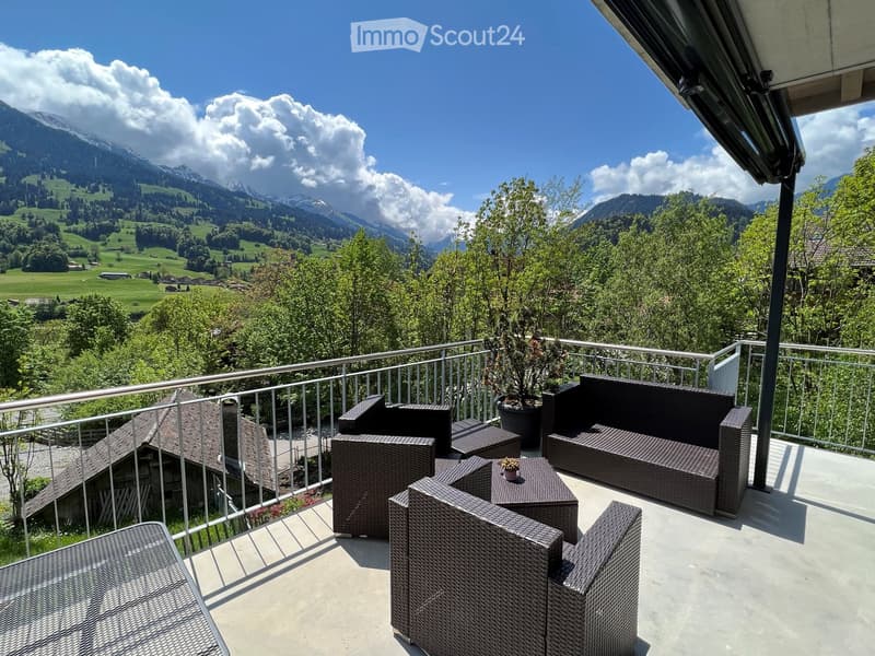 Balcony with wicker furniture, including a sofa, chairs, and a small table, overlooking a scenic mountain landscape.