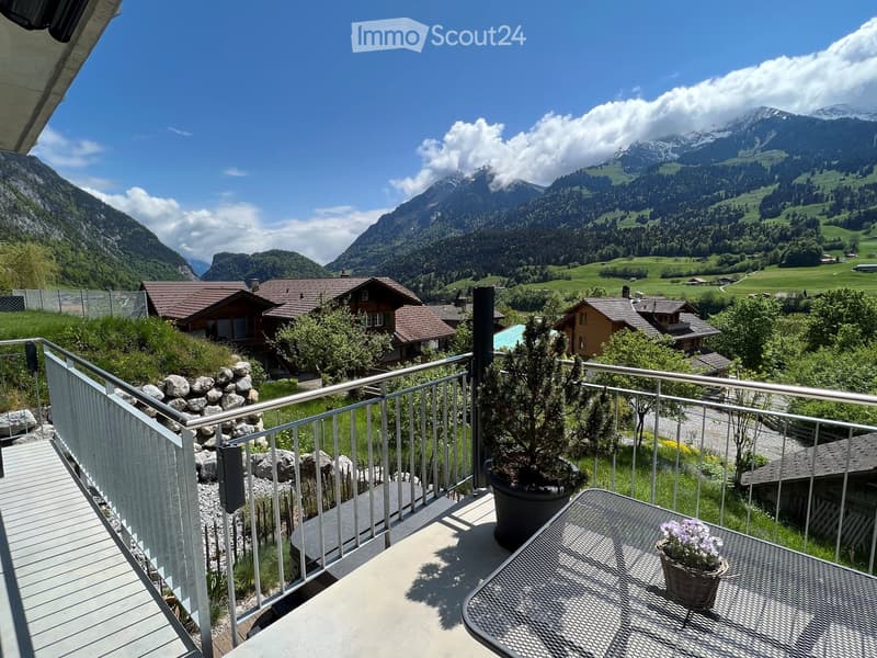 Balcony with a metal railing, a round metal table with a potted plant, and a scenic mountain view.