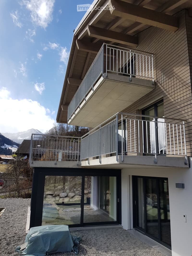 Modern two-story house with balconies, large windows, and a scenic mountain view in the background.