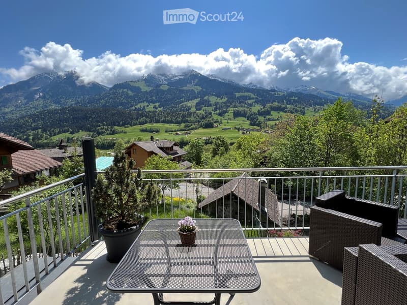 Balcony with a scenic mountain view, featuring a metal table, wicker chairs, and potted plants.