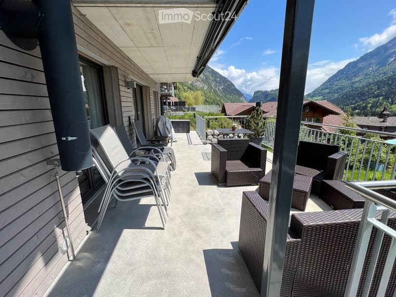 Balcony with outdoor furniture including chairs, a table, and ottomans, overlooking a scenic mountain view.