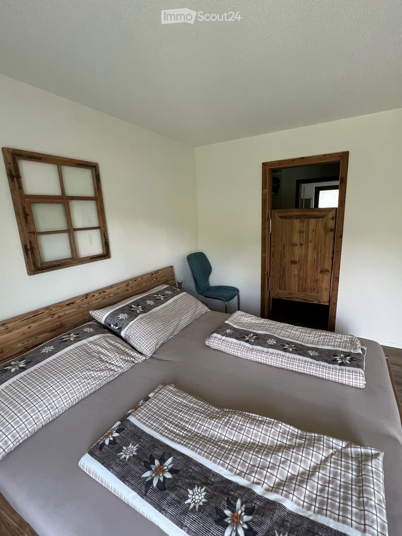 Cozy bedroom with a wooden bed frame, patterned bedding, and a single blue chair near the door.