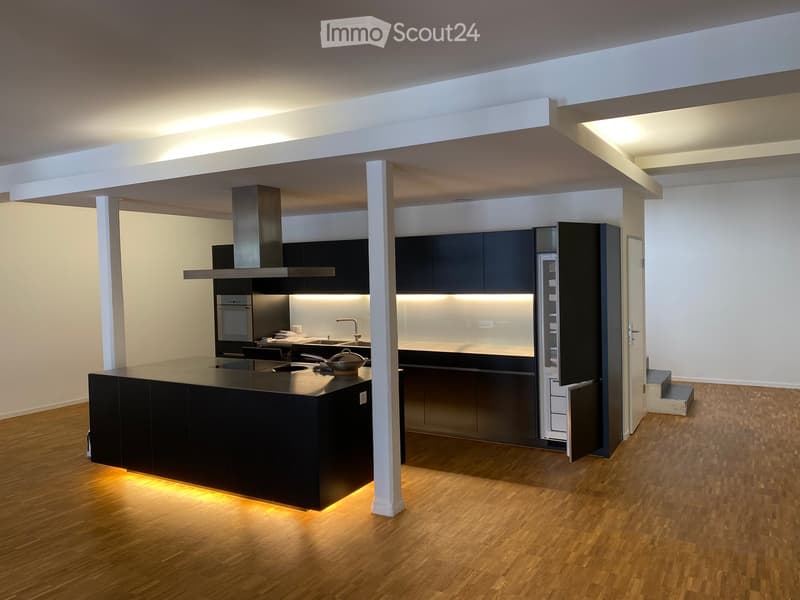 Modern kitchen with dark cabinets, a central island, built-in appliances, and sleek lighting.