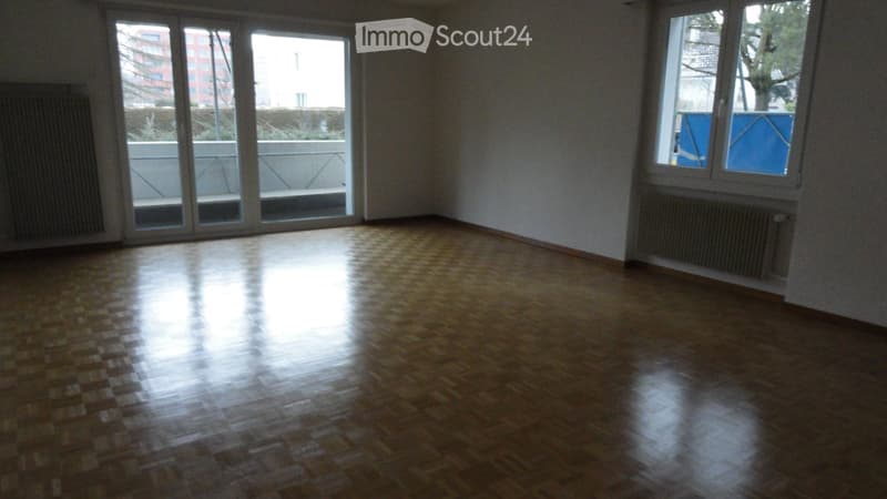 Empty room with wooden flooring, large windows, and radiators on both sides.