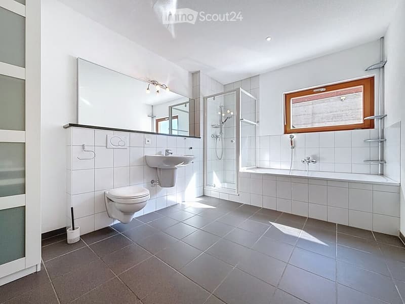 Modern bathroom with white tiles, a toilet, a sink, a bathtub, and a glass-enclosed shower. Features a large mirror above the sink and a window with wooden frame.