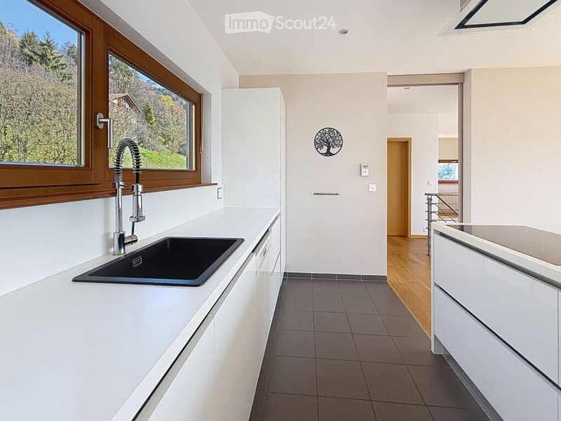 Modern kitchen with white cabinets, black sink, and large window offering a scenic view of greenery.