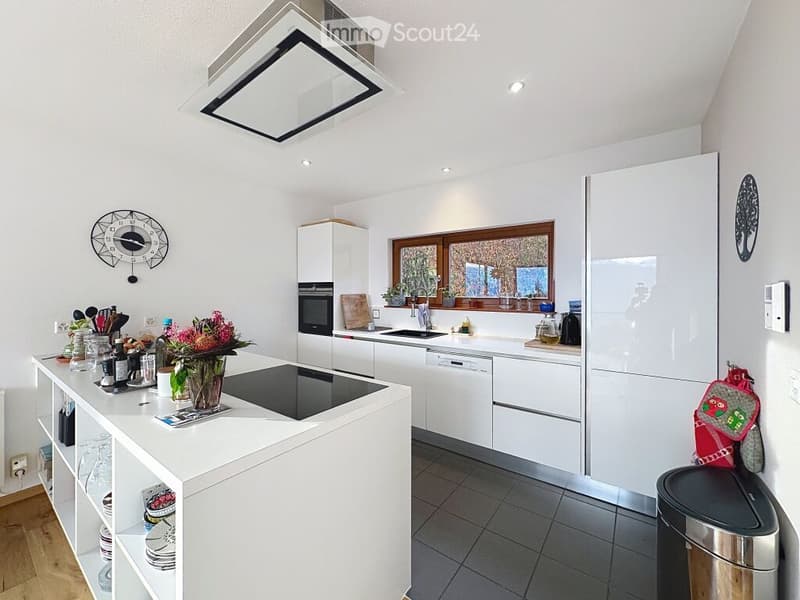 Modern kitchen with white cabinets, stainless steel appliances, island with induction cooktop, and various kitchen items on counters.
