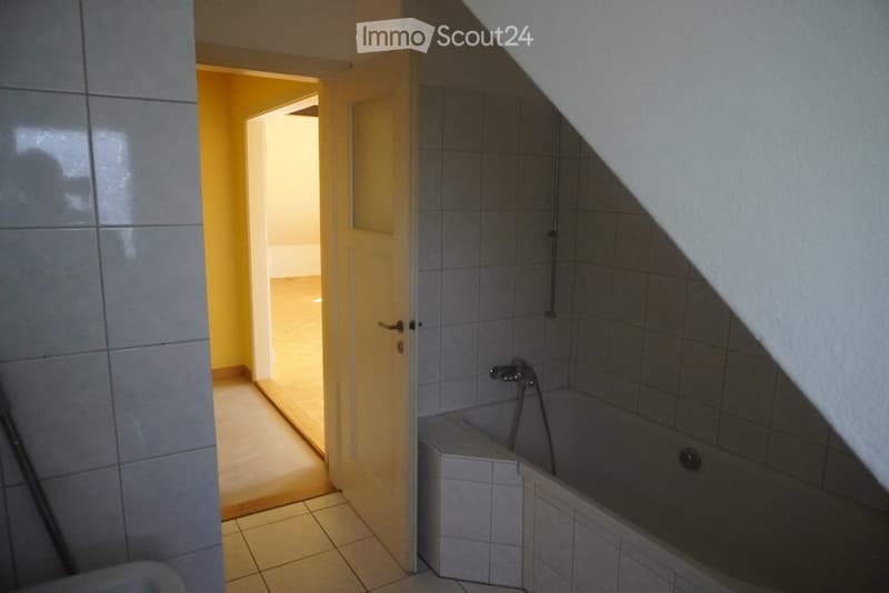Bathroom with tiled walls and floor, featuring a bathtub with a faucet and a door leading to another room.