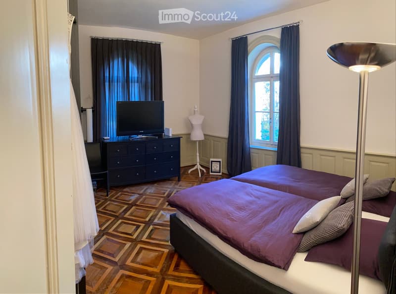 Cozy bedroom with two single beds, dark wooden dresser, television, floor lamp, and decorative mannequin.