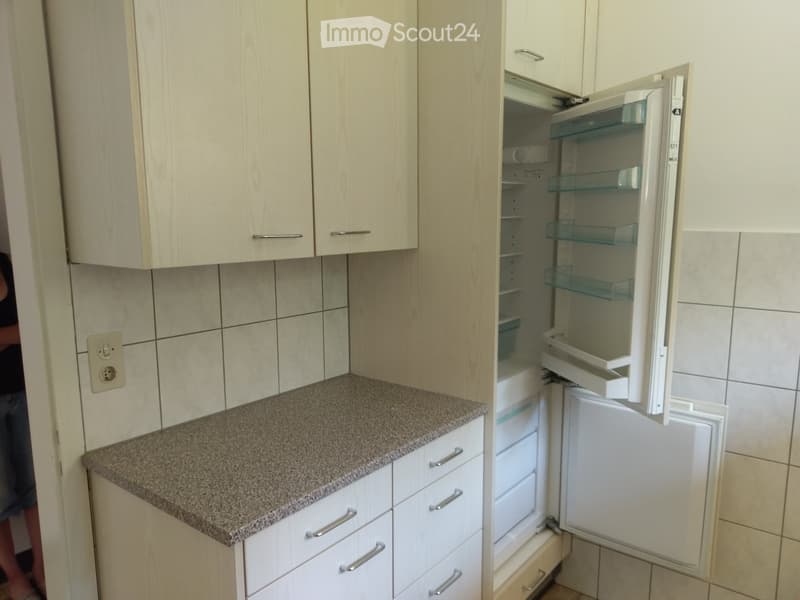 Modern kitchen with light wood cabinets, granite countertop, and an open refrigerator with glass shelves.