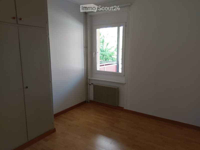 Empty room with wooden flooring, white walls, a window with blinds, and a radiator below the window.