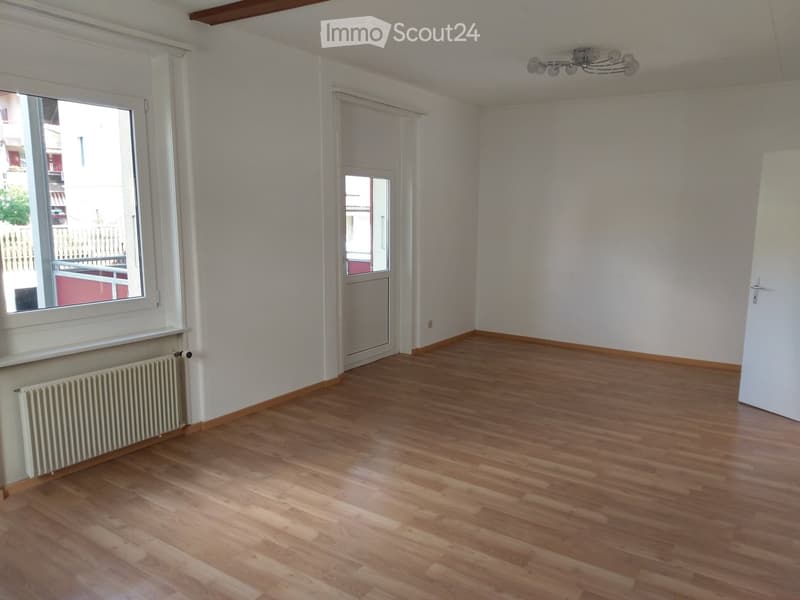 Empty room with wooden flooring, white walls, a radiator, and a window with a view of a balcony.