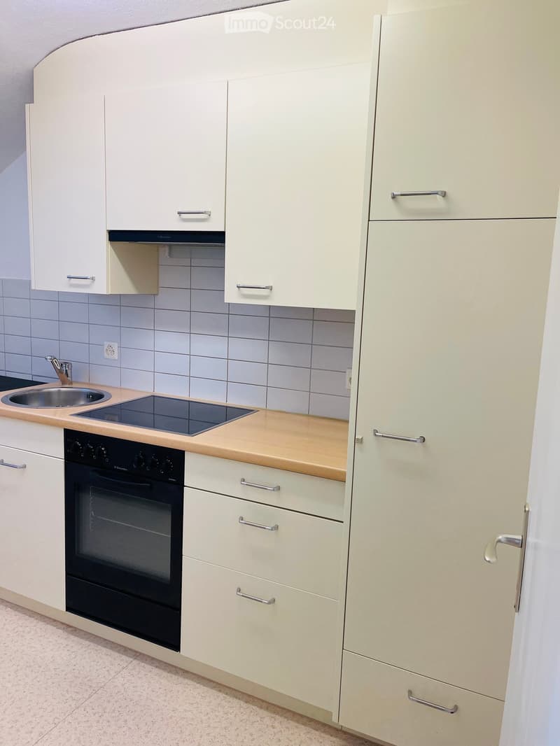 Clean modern kitchen with white cabinets, wooden countertops, induction cooktop, built-in oven, stainless steel sink, white tiled walls, white floors, power outlet