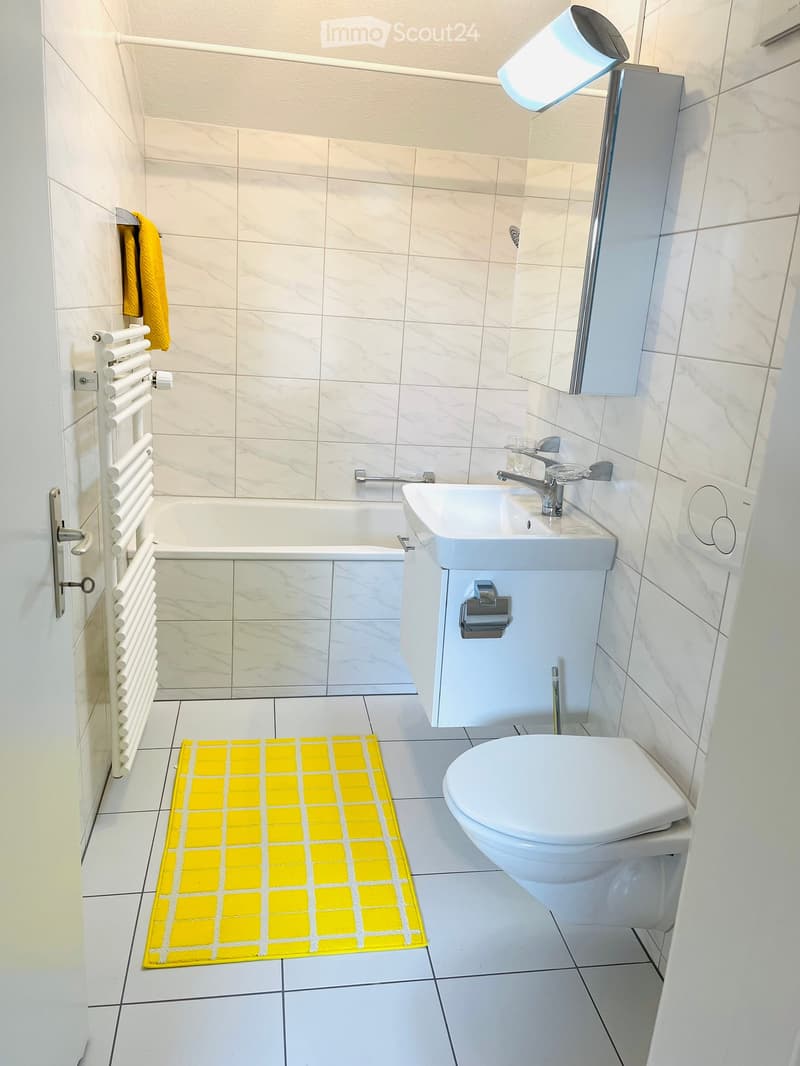 white tiles, bathtub, sink, toilet, towel rack, mirror, white radiator, yellow mat