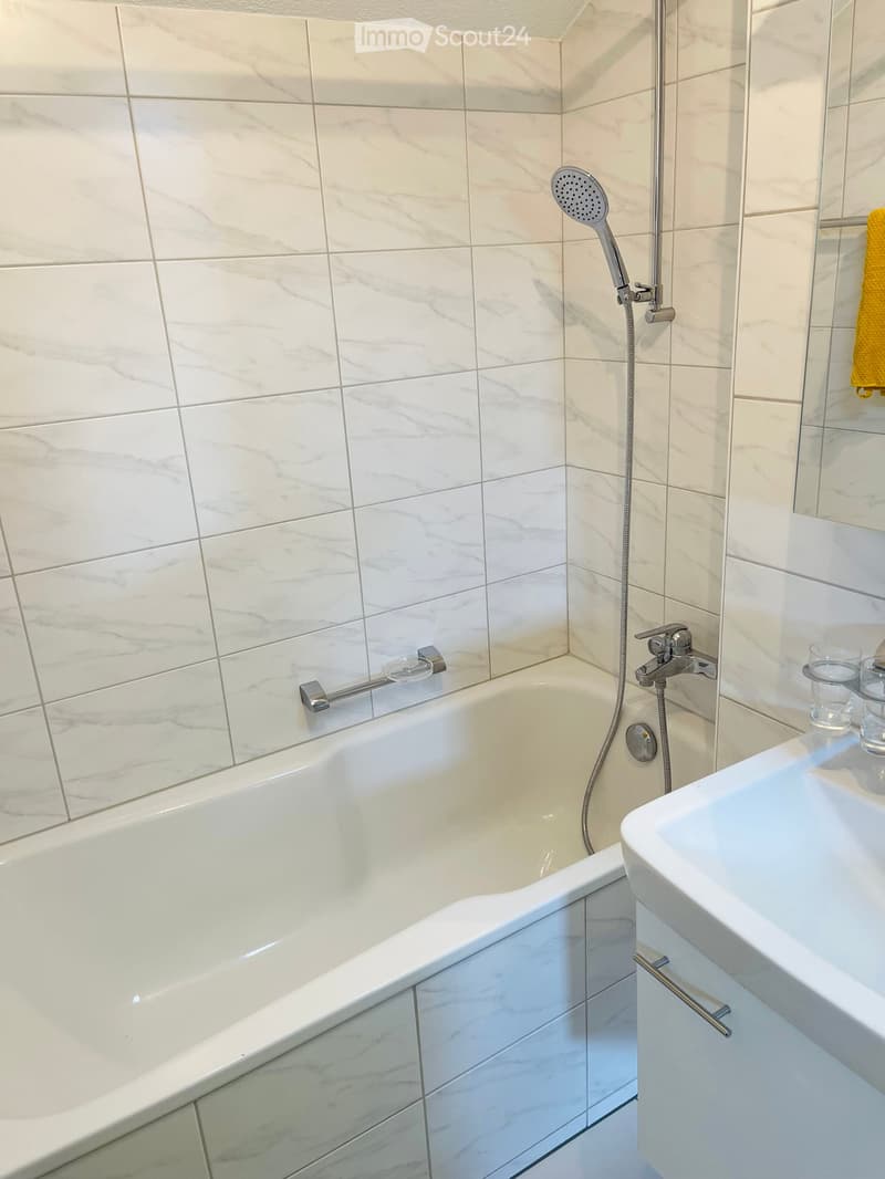 modern bathroom with white tiles, bathtub, shower, and sink