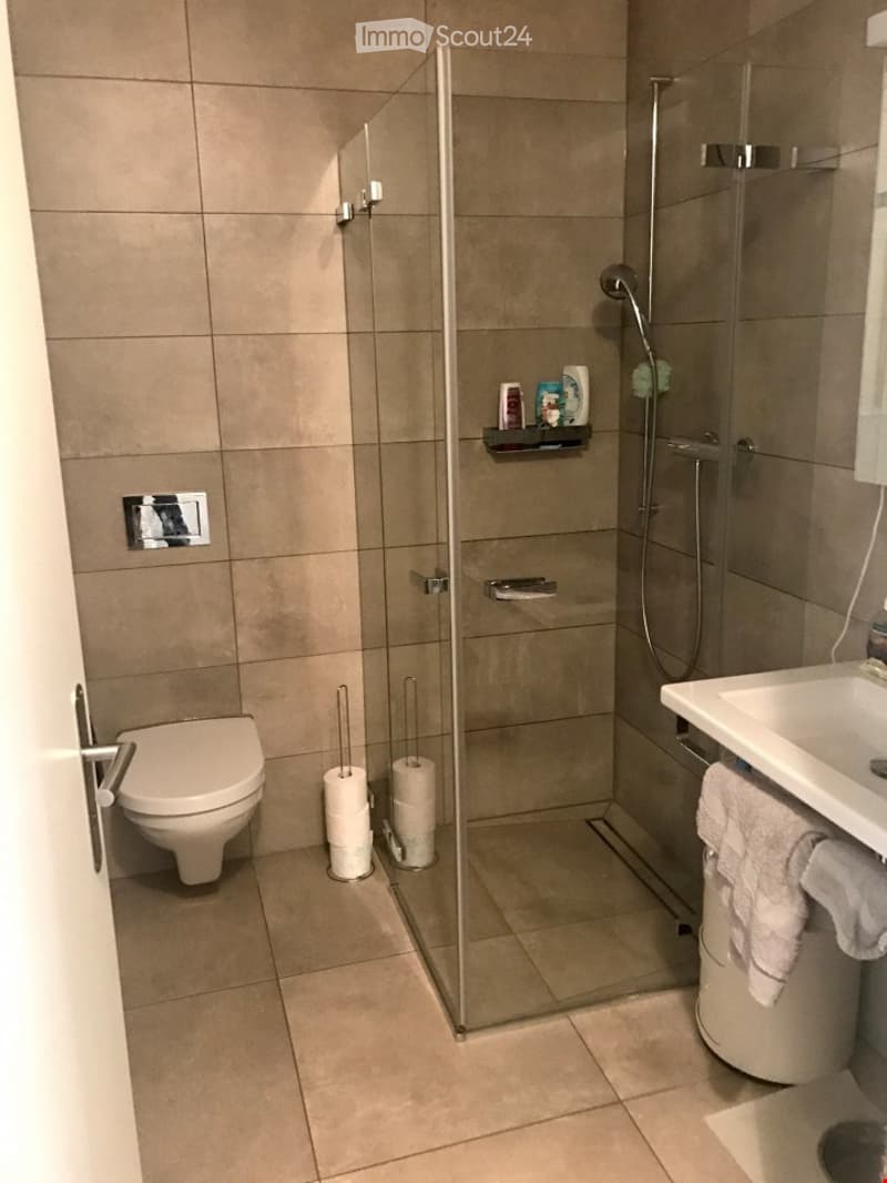 Modern bathroom with a glass shower enclosure, white toilet, white sink, and tiled floor.