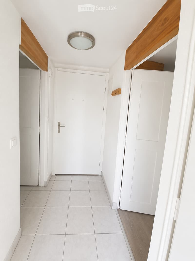 Clean, modern hallway with white tiled flooring, white walls, and wooden trim. Features a central ceiling light fixture and multiple white doors.