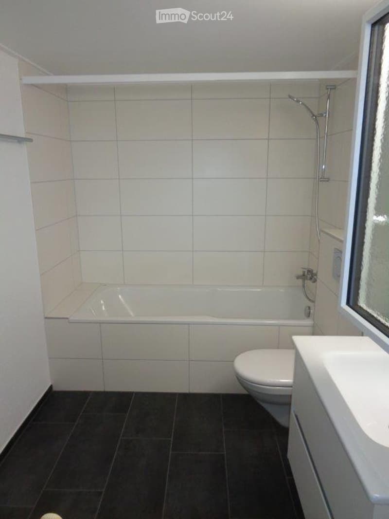 Modern bathroom with white tiled walls and black tiled floor, featuring a bathtub, toilet, sink, and shower.