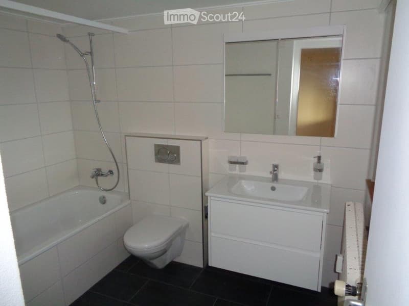 Modern bathroom with white tiles, bathtub, toilet, sink, mirror, and showerhead.